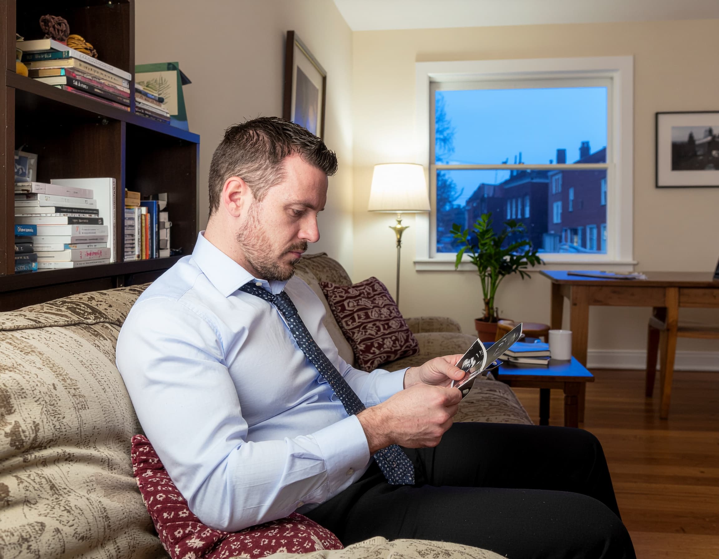 An expectant father sits on a couch, quietly looking at an ultrasound photo.