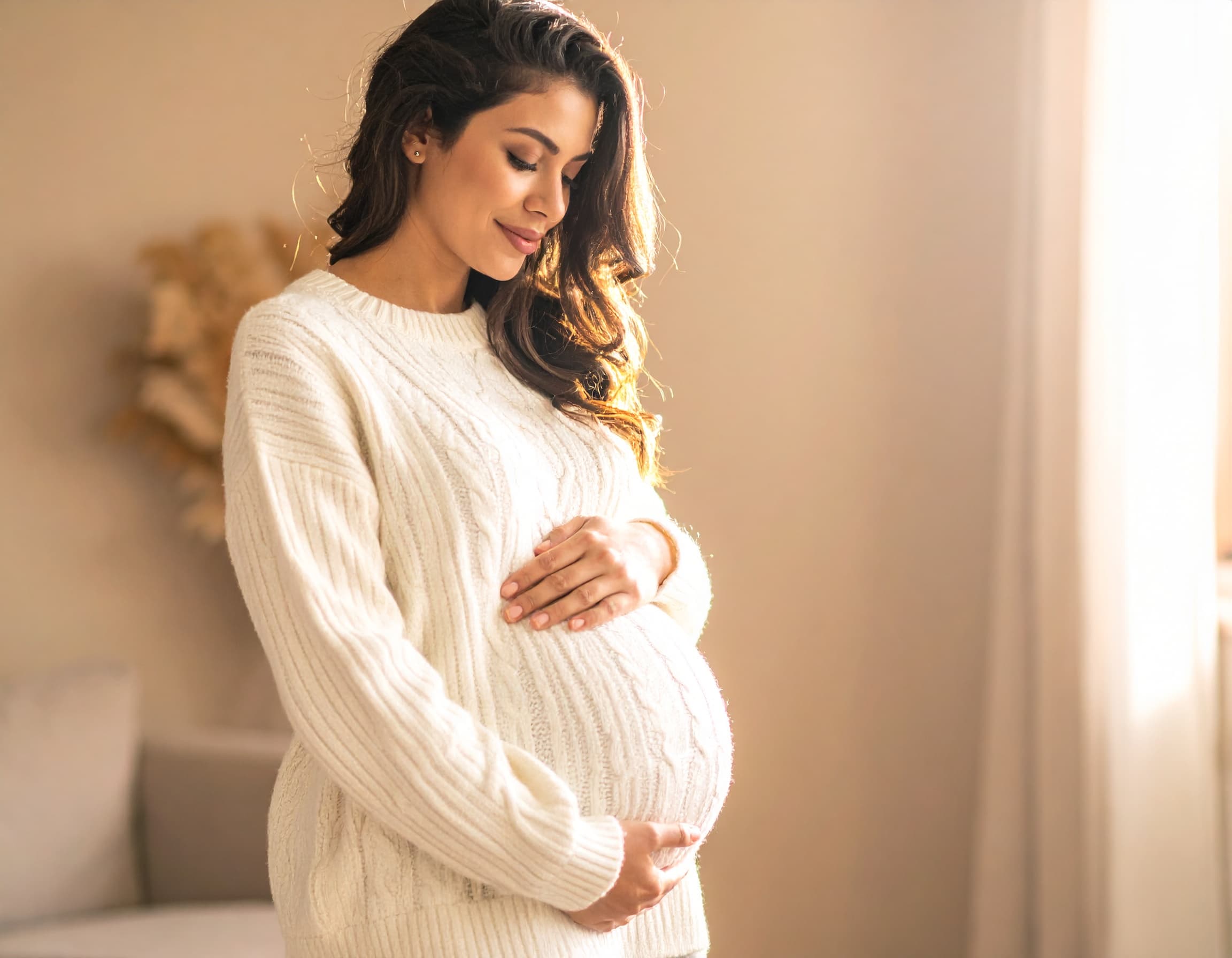 An expectant mother cradles her belly in warm light.